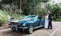 Newly-weds posing for photo’s along side the East Coast Blue Shelby 1965 Mustang